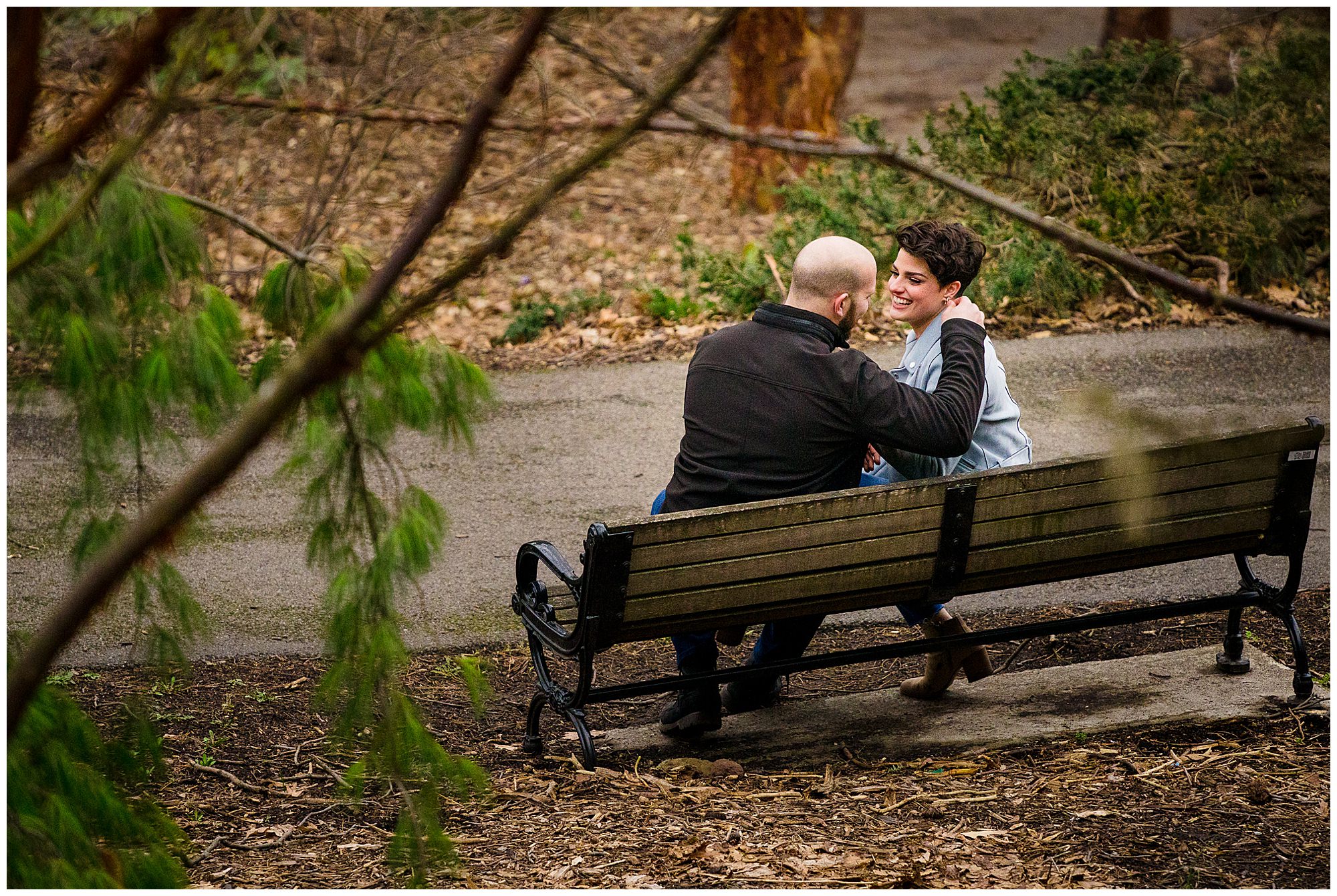 A newly engaged couple sit on a bench in highland park.