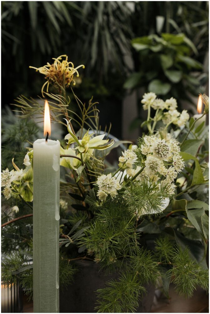 Lit green candle with lush floral arrangement