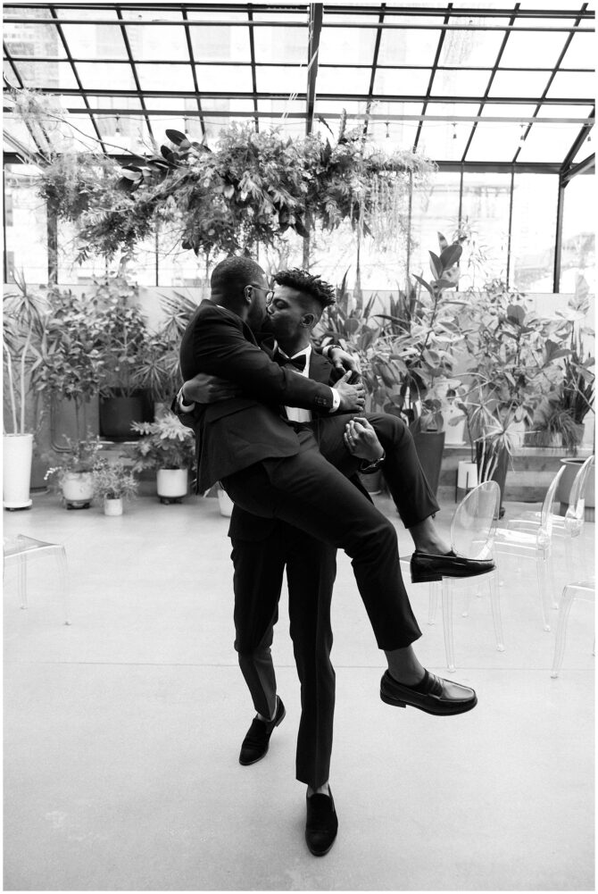 Two men embracing in a lush indoor setting.