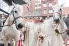 Couple kisses beside two horses at wedding event.