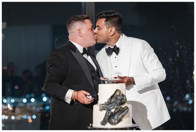 Couple kissing beside cake at wedding reception.