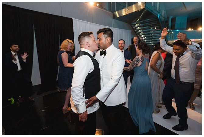 Wedding couple kissing surrounded by dancing guests.