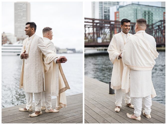Grooms holding hands by a waterfront in traditional attire.
