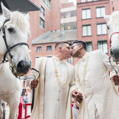 Couple kisses beside two horses at wedding event.
