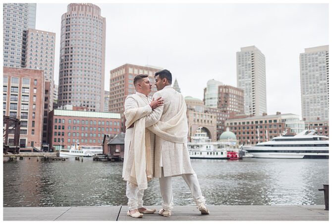 Couple in traditional attire by waterfront cityscape.