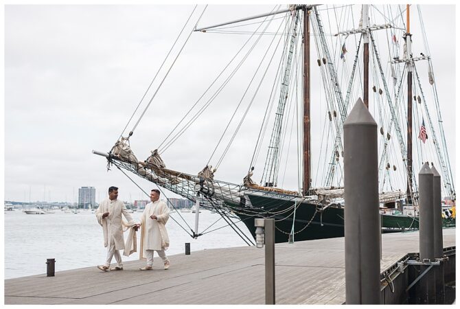 Two people in traditional attire by a sailboat.