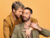 Two men in stylish suits embrace warmly.