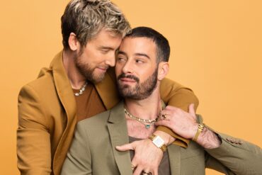 Two men in stylish suits embrace warmly.