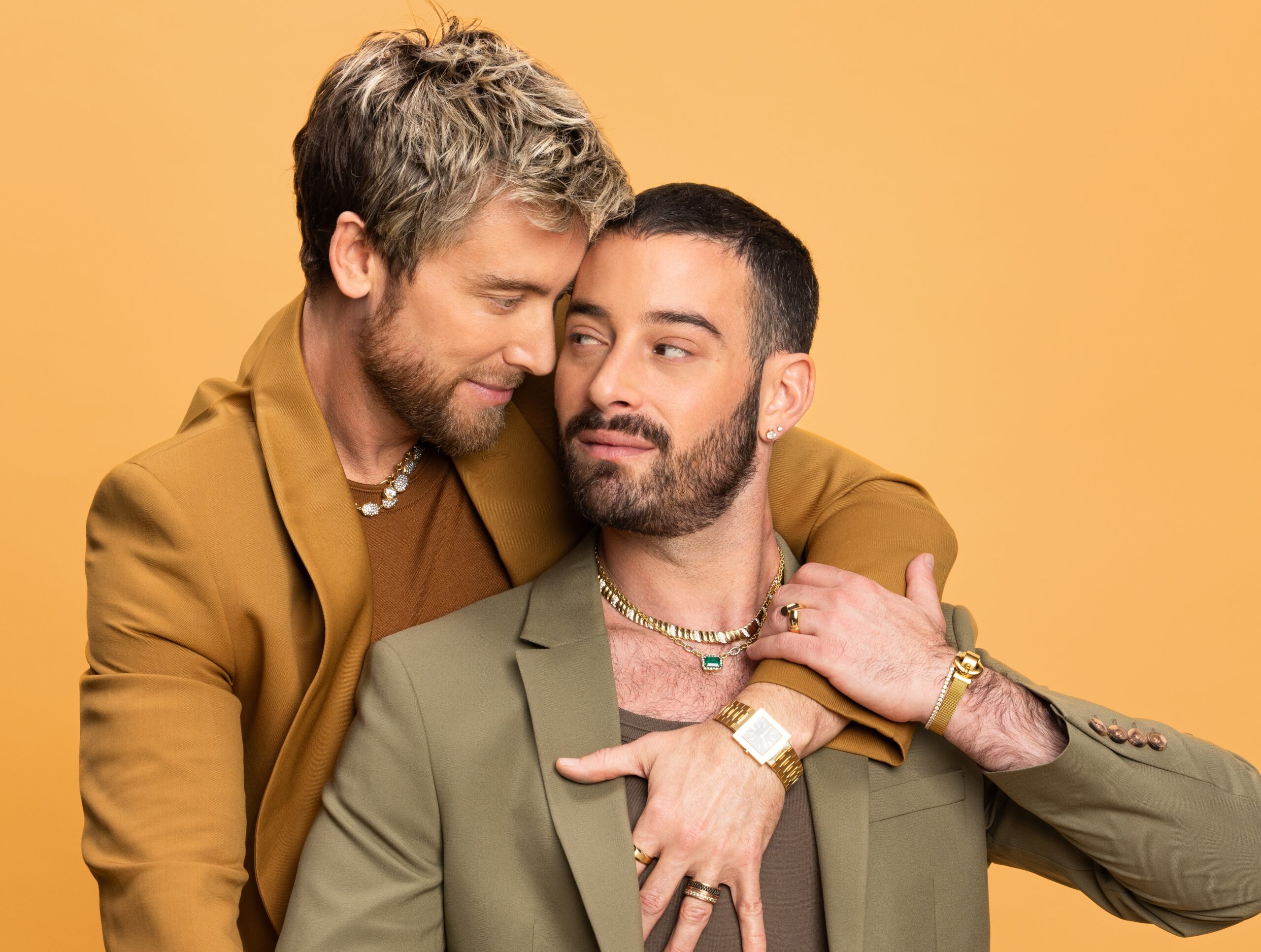 Two men in stylish suits embrace warmly.