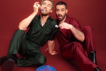 Two people in colorful outfits with a cake.