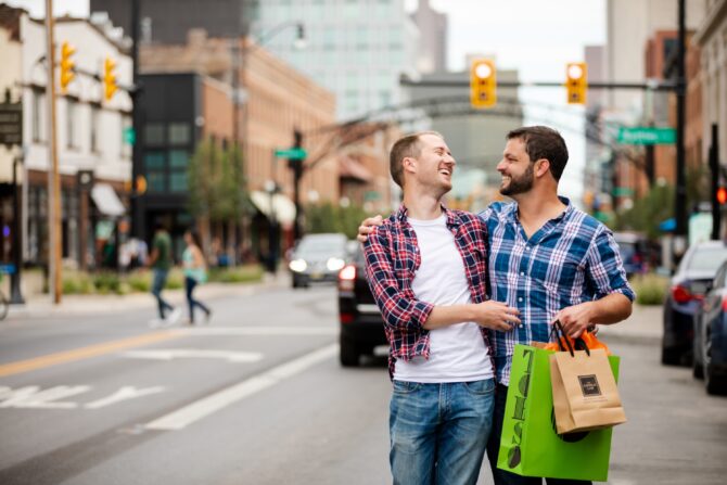 Two friends laughing with shopping bags in city street.