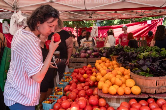 Woman selects tomatoes at outdoor farmers market.