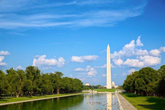 Washington Monument reflecting pool and trees under blue sky.