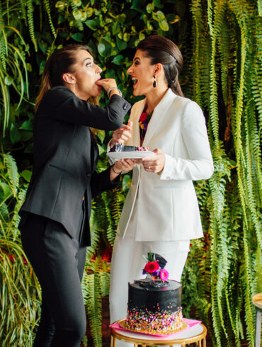 Two women sharing cake, surrounded by greenery.