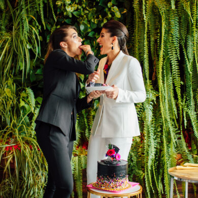 Two women sharing cake, surrounded by greenery.