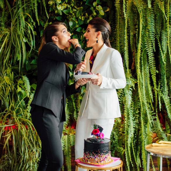 Two women sharing cake, surrounded by greenery.