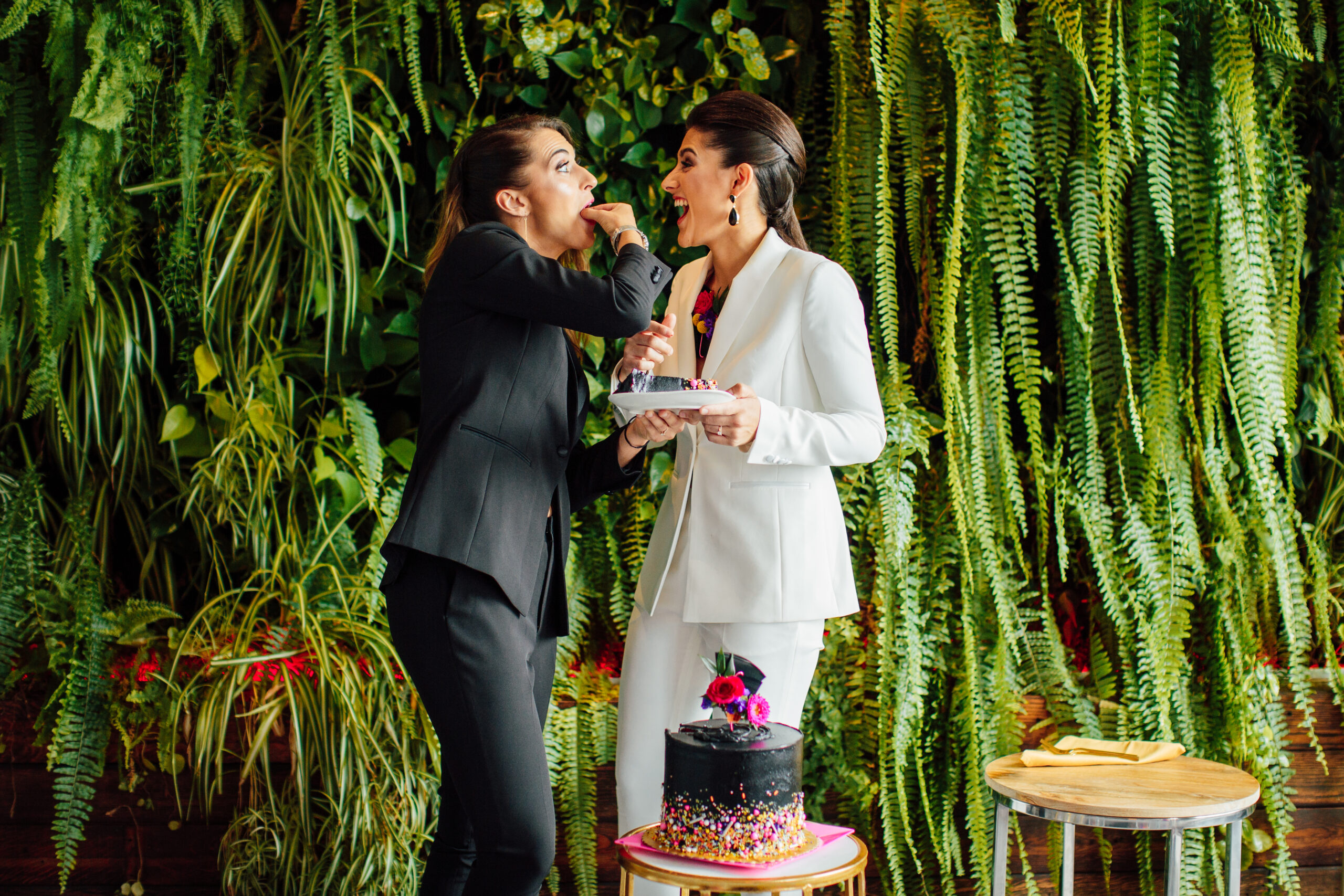 Two women sharing cake, surrounded by greenery.
